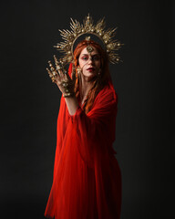 dramatic close up portrait a female model wearing a red silk dress and veil robes, with a ornate golden fantasy crown headdress. isolated on a dark studio background with  silhouette rim lighting 