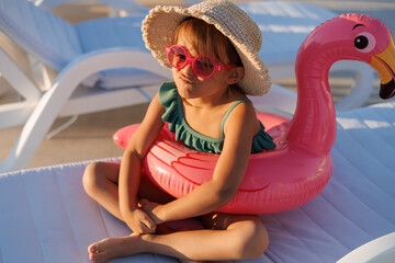 Cute funny toddler girl in a sunglasses relaxing on inflatable toy ring floating in pool have fun during summer vacation. Child having fun in swimming pool.