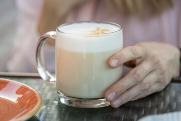 A woman holds a glass of coffee with a white foam on top