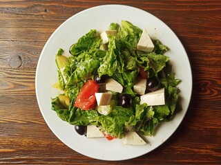 Beautiful Greek salad on a white plate, on a wooden table. European cuisine.