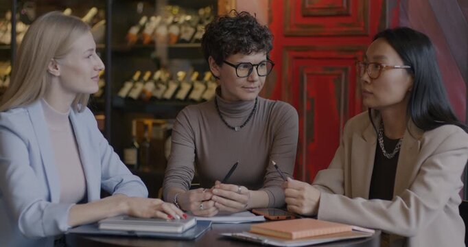 Young businesswomen Asian and Caucasian talking during negotiations with interpreter in cafe. International business and translation service concept.