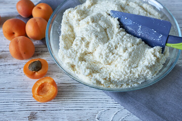 Cooking apricot pie on a white wooden background. Dough in a bowl and apricots on the table.