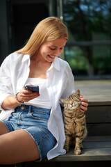 pretty smiling middle-aged European woman with blonde hair sitting on the stairs using a smartphone...