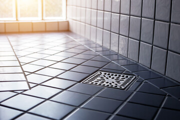 Square shower drain new and clean in tiled floor of modern enclosure in bathroom. New restroom tile floor clean and dry in house.