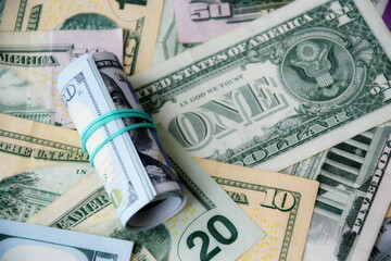 Hundred dollar bills roll lies on big amount of US dollars in different nominations under natural light