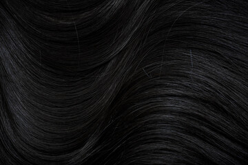 Brunette or black hair. Female long dark hair in black. Beautifully laid curls. Closeup texture in a dark key. Hairdressing, hair care and coloring. Shading gray hair. Background with copy space.