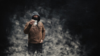 Drug dealer, dangerous hooded criminal man in black mask and brown leather jacket holding...