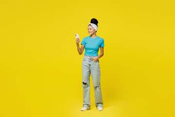 Fototapeta premium Full body young Latin woman wears blue top t-shirt headband casual clothes hold in hand use mobile cell phone typing message chat online isolated on plain yellow background studio. Lifestyle concept.