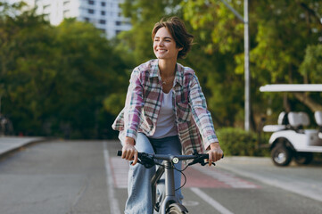 Side view young happy cool woman wear checkered shirt casual clothes look aside walk riding bicycle...