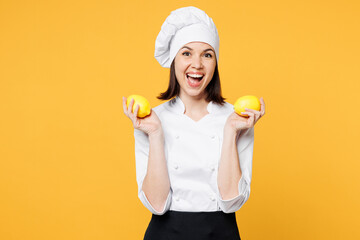 Young surprised shocked chef cook baker woman wear white shirt black apron uniform toque chefs hat hold in hand two lemons look camera isolated on plain yellow background studio. Cooking food concept.