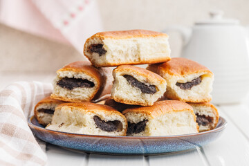 Sweet bun with poppy seed on plate on white table.