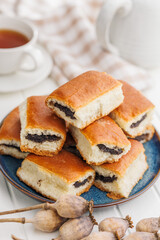 Sweet bun with poppy seed on plate on white table.