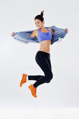Jump, woman and dance by studio for workout, balance and flexibility with movement for wellness. Girl, fitness and training for cardio health with aerobic exercise, endurance and white background