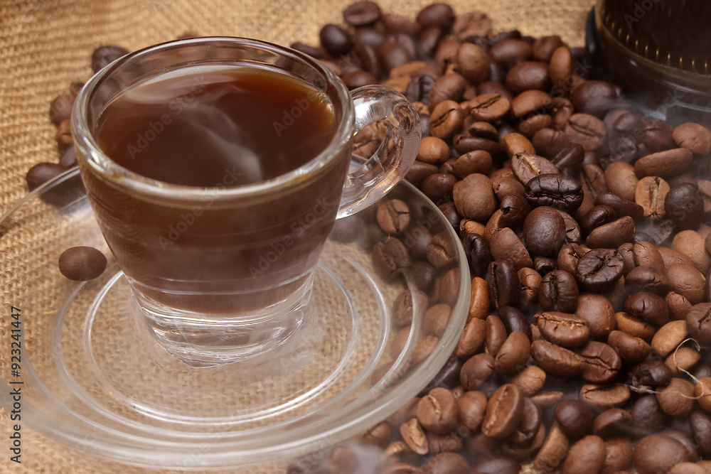 Wall mural Dark brown Coffee bean macro closeup flow move fall drop pan roll smoking roasting cooking transparent clear glass cup saucer pour liquid on jute fabric background