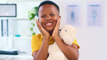 Smiling Child Holding a Teddy Bear in a Bright Office Setting, Expressing Joy and Comfort with...
