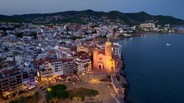 Night aerial view of Costa Brava in Spain, coastal Spanish village of Sitges drone view in the evening, mediterranean holiday resort in Spain with medieval church at night