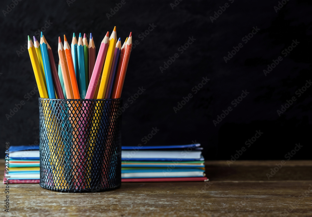 Aufkleber Colored pencils standing in a cup on a wooden desk with books and a blackboard as background for an educational concept