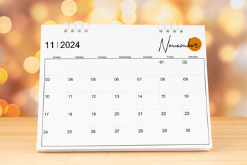 November 2024 desk calendar on wooden table with gold light bokeh background.