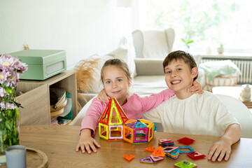 Cute children, brother and sister, assemble magnetic constructor at home at the table. Educational games for children. happy