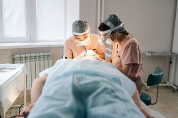 Focused two female doctors collecting hair follicles from donor area of patient for hair...