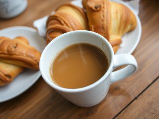 Obraz premium Freshly Brewed Coffee with Croissants A close-up of a cup of freshly brewed coffee with steam rising, accompanied by golden, flaky croissants on a wooden table. The setting is warm and inviting, perfe