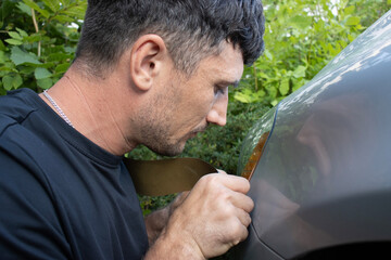 European man repairing a car. Puttying scratches on paint. Sanding with sandpaper. Service at a...