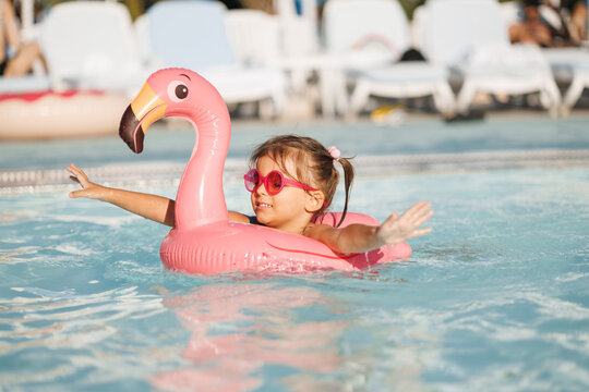 Cute funny toddler girl in a sunglasses relaxing on inflatable toy ring floating in pool have fun during summer vacation. Child having fun in swimming pool. 