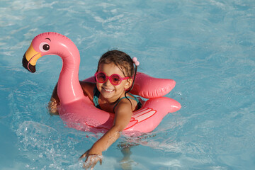 Cute funny toddler girl in a sunglasses relaxing on inflatable toy ring floating in pool have fun...
