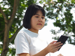 Asian businesswoman walking in outdoor park, reading business text, using smartphone to send text and reply to electronic messages.