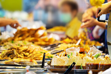 A group of people are gathered around a buffet table with a variety of food. The atmosphere is casual and social, with people mingling and enjoying the food
