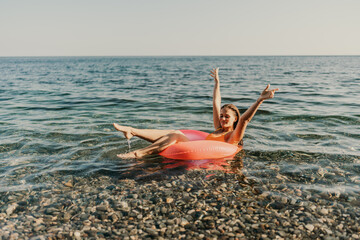 A woman is floating on a pink inflatable tube in the ocean