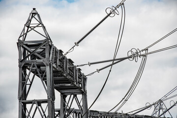 Power cables and pylon structures, against a cloudy sky. Steel articulated frames distribute...