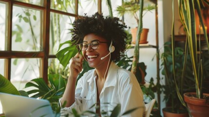 Fototapeta premium A woman with a bright smile wears a headset, working amidst a lush array of plants in her vibrant home office.