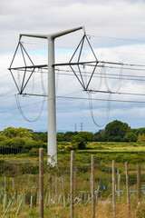 Fototapeta premium T-Pylon, Power cables and pylon structures, against a cloudy sky. Steel articulated frames distribute electricity to the national grid.
