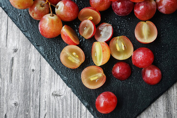 A bunch of large pink grapes next to cut grapes on a black tray on a gray wooden background
