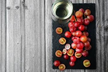 A bunch of large pink grapes next to a glass of white wine on a black tray on a gray wooden background