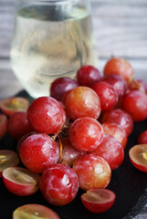 A bunch of large pink grapes next to a glass of white wine on a black tray on a gray wooden background