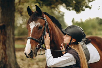 Obraz premium A young female equestrian stands near her horse and prepares for a competition.