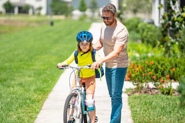 Fototapeta premium Fathers day. Boy learning to ride a bicycle with his father in park on summer day. Father teaching his son cycling on bike. Father learn little son to ride a bicycle. Father support kid. Happy Fathers