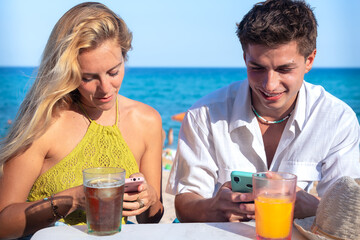 Two young happy friends in a restaurant using applications on smartphones.