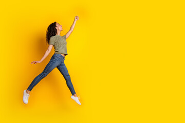 Full size photo of positive girl dressed striped t-shirt jeans run look empty space hand catch object isolated on yellow color background
