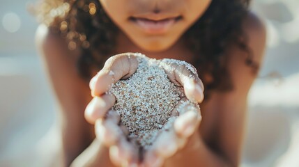 Naklejka premium Close-up of a child gently holding a handful of sand, capturing the simplicity and innocence of childhood moments at the beach.