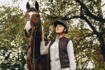 A young female equestrian stands near her horse and prepares for a competition.