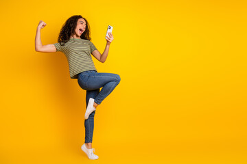 Full size photo of satisfied girl with wavy hair dressed striped t-shirt look at smartphone win bet...