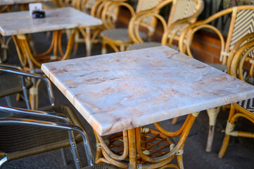 Group of chairs and tables on the sidewalk in front of a café.