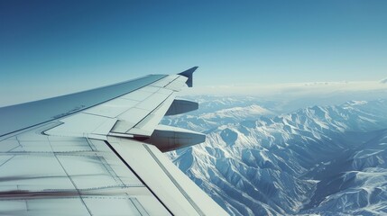 Fototapeta premium The wing of an airplane soars over a vast, snowy mountain range under a bright, clear sky.