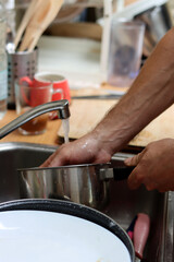 Close up photo of male hands doing dishes. Running water, dishes in sink. Water saving concept. 