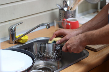 Close up photo of male hands doing dishes. Running water, dishes in sink. Water saving concept. 