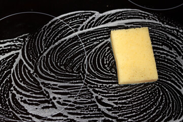 Cleaning the gas stove with foam and sponge. Sponge on a black kitchen stove, close-up photo of wet...