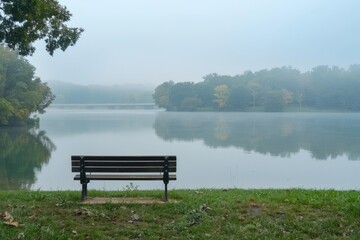 Fototapeta premium Empty park bench overlooking tranquil lake on quiet morning